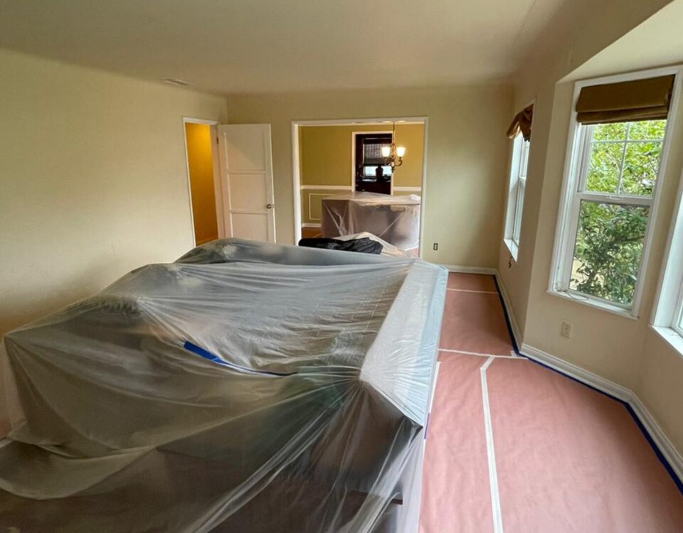 Furniture moved to the center of the room and wrapped in plastic, with rosin paper taped down over the floor before interior painting starts