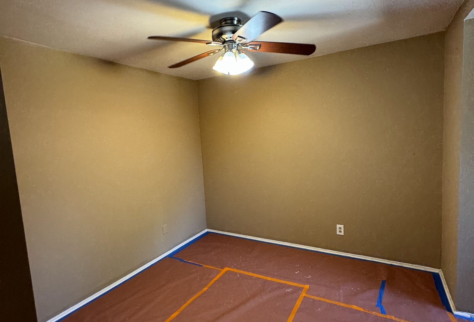 Bedroom mid-job with the walls repainted and the ceiling left in its original color, floor covered in rosin paper and the baseboards taped off