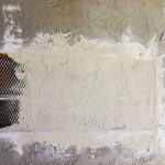 Stucco wall opened up for a full three-coat repair, with the metal lath and building paper visible behind the removed section