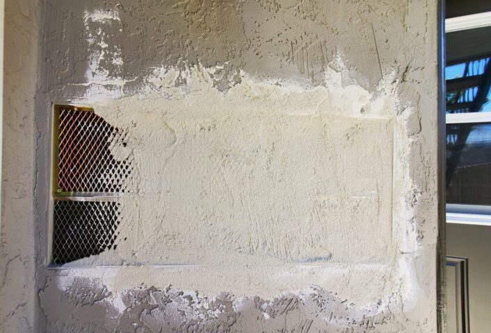 Stucco wall opened up for a full three-coat repair, with the metal lath and building paper visible behind the removed section