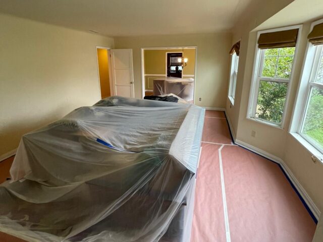 Furniture wrapped in plastic and red rosin paper protecting the floor before interior painting