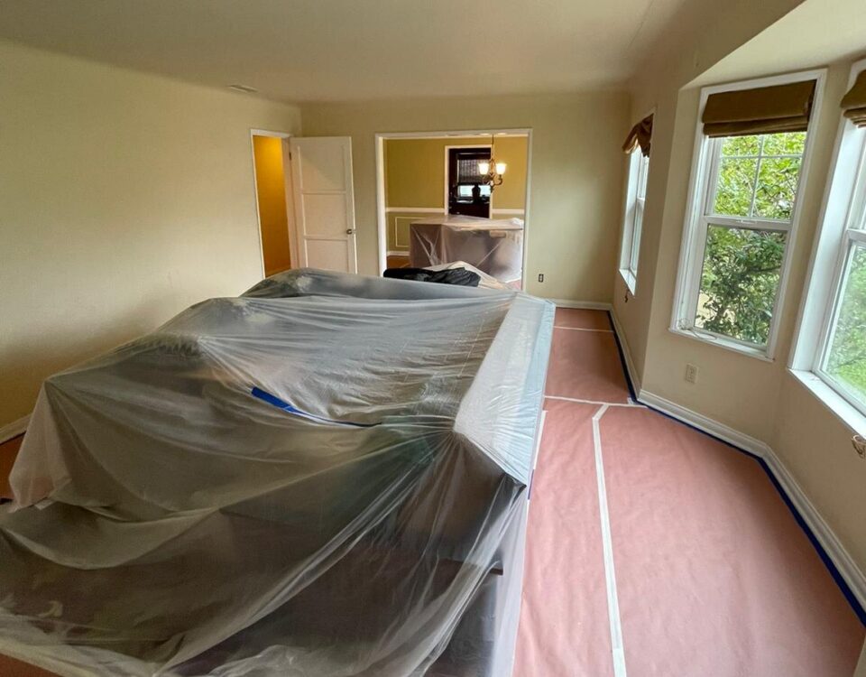 Furniture wrapped in plastic and red rosin paper protecting the floor before interior painting