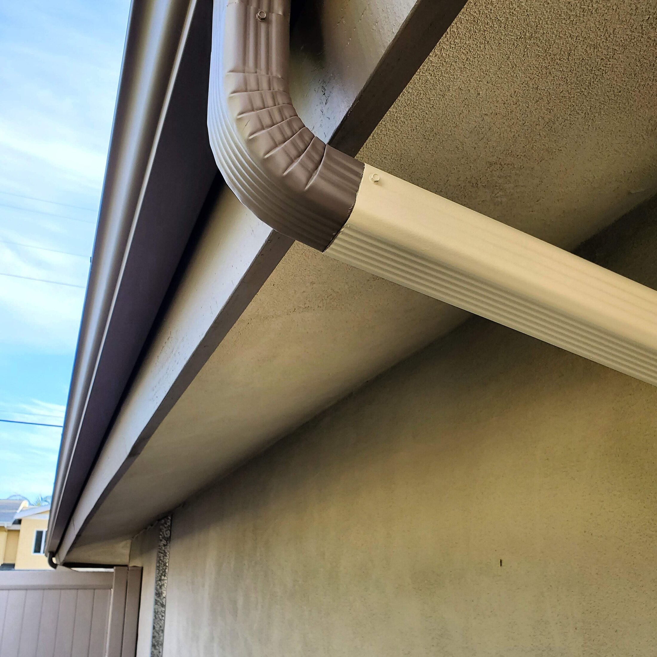 Close view of a brown rain gutter and downspout elbow installed under a San Diego roof edge