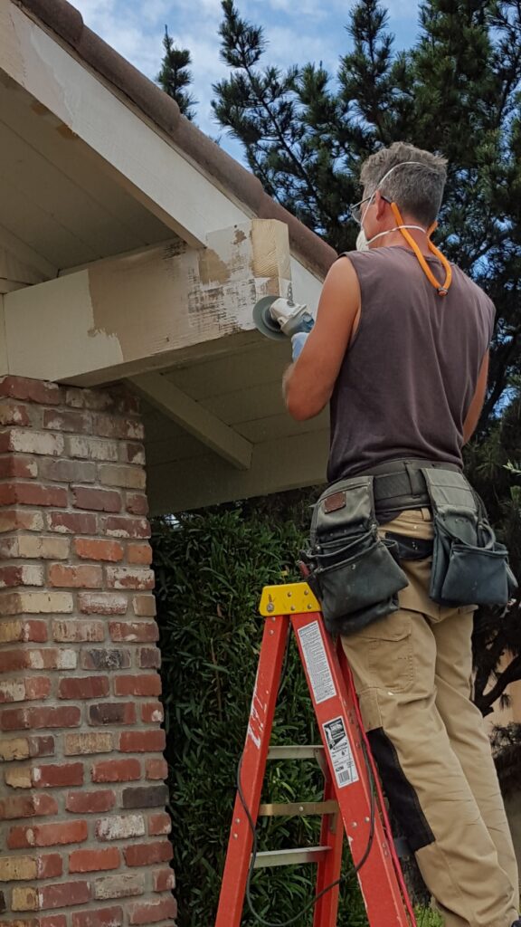 Painter using an orbital sander on exterior fascia before primer and paint