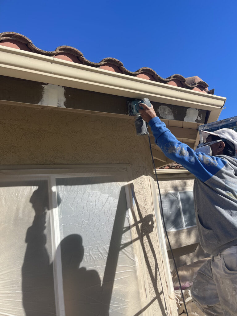 Painter sanding fascia near an attached gutter after localized wood preparation